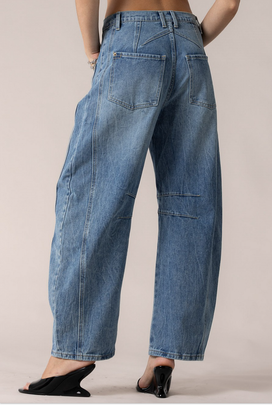Back three-quarter close-up of denim pockets and contoured yoke on barrel-leg jeans.
