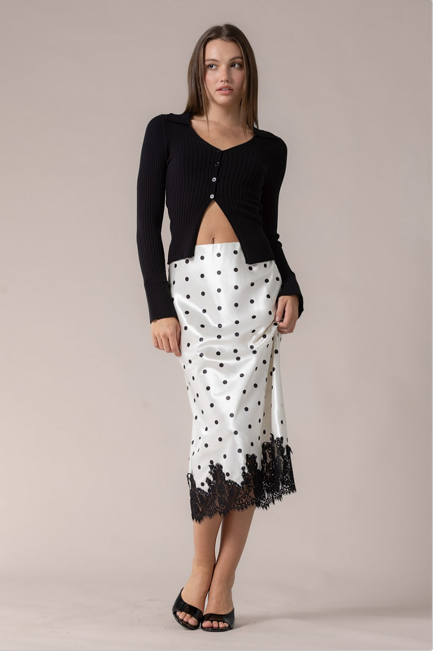Full outfit view of model wearing black cardigan and white polka dot lace slip skirt