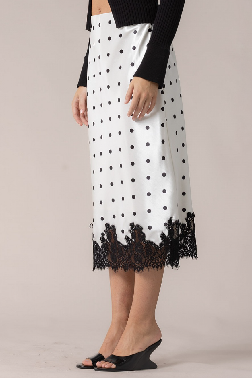 Side view of polka dot slip skirt in white satin with black lace hem on model
