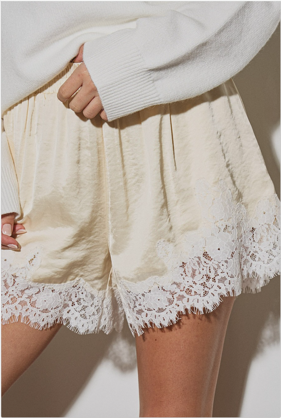 Close-up of butter yellow satin shorts with lace-trim hem detail.
