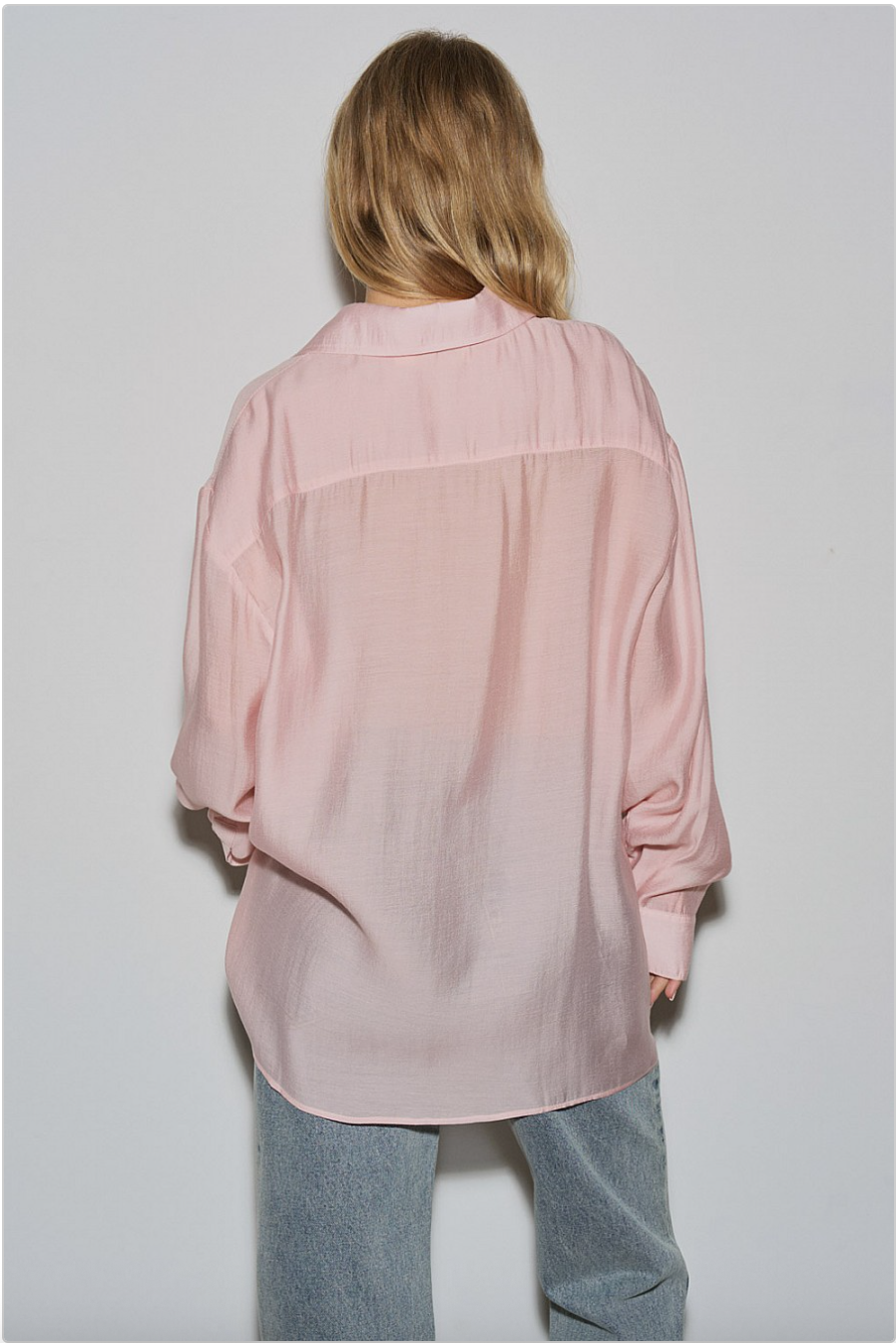 Full back view of blush pink oversized sheer button-down shirt with long sleeves and curved hem, paired with jeans.