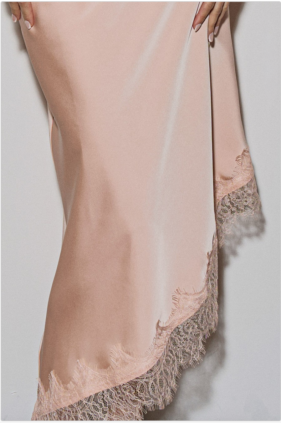 Detail view of peach satin-like fabric and lace-trimmed high-low hem.