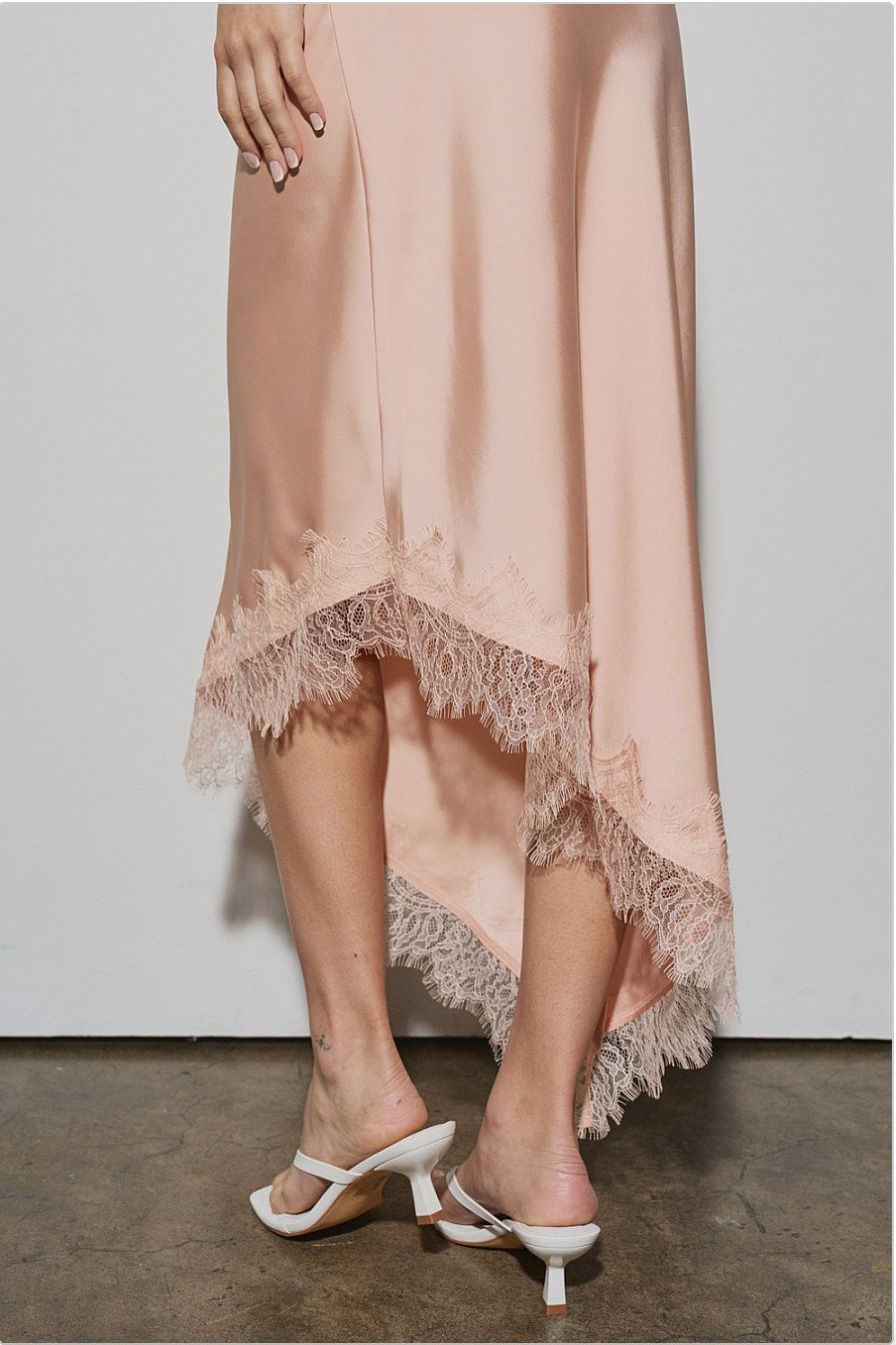 Back view of peach asymmetrical skirt with lace-trim high-low hem, styled with white heels.