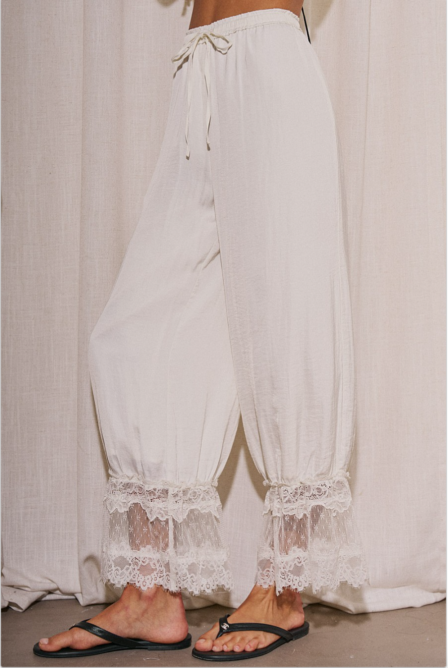 Side view of ivory billowy pants with gathered lace hem detail