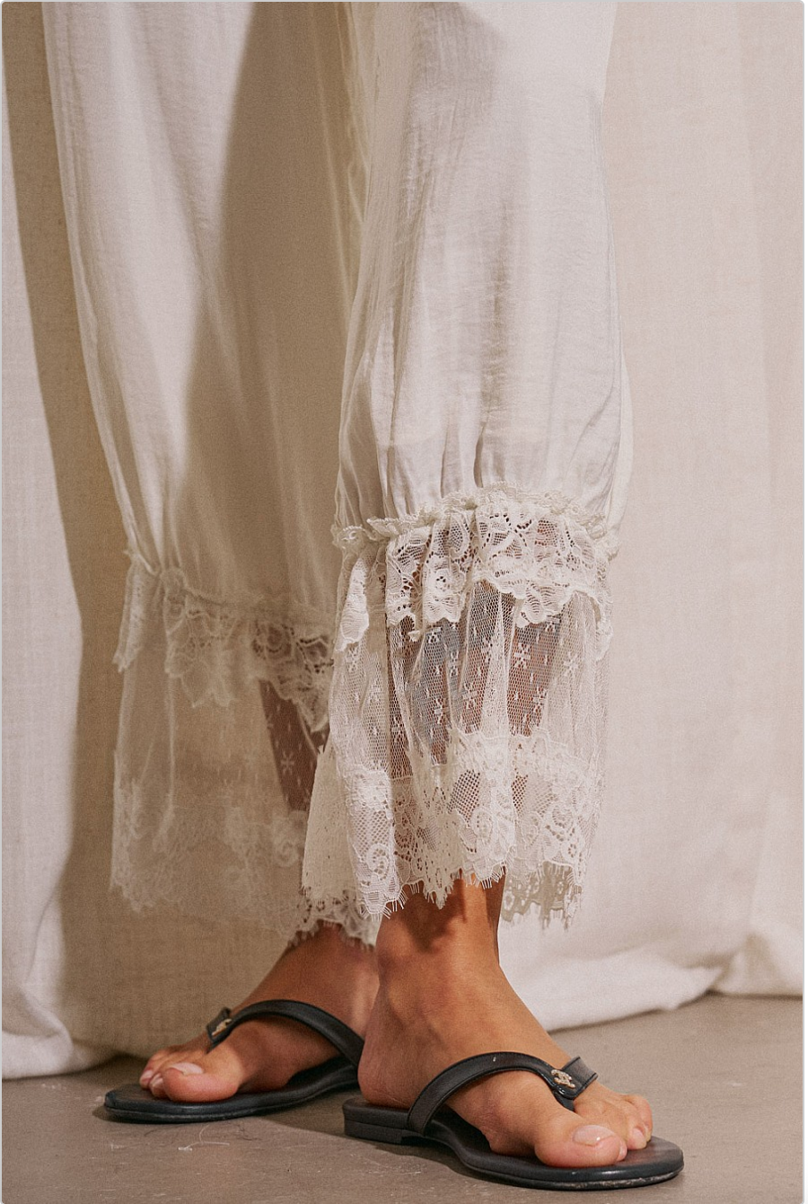 Close up of white lace hem resort pants with drawstring waist and soft billowy fit