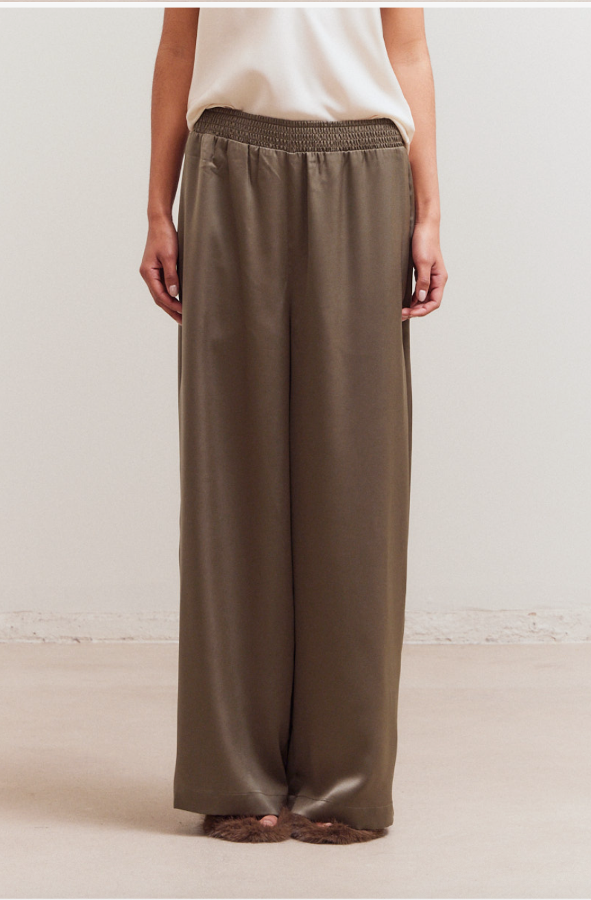 Close up of olive satin palazzo pants showing smocked waistband, soft sheen, and fluid wide leg
