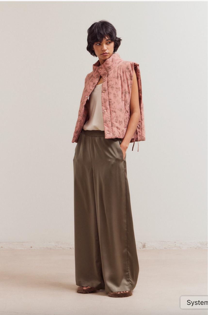 Model wearing olive smocked waist satin palazzo pants styled with a pink quilted vest and ivory camisole