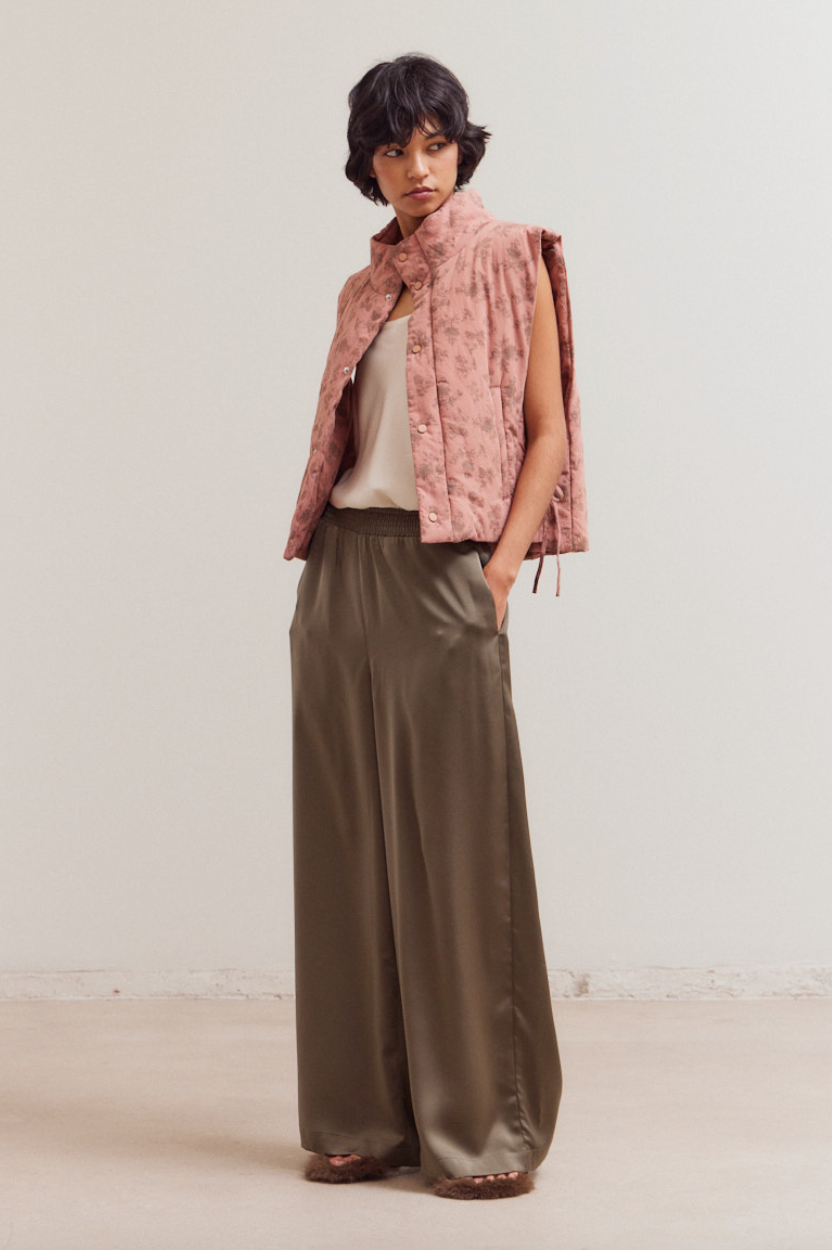 Model wearing olive smocked waist satin palazzo pants styled with a pink quilted vest and ivory camisole